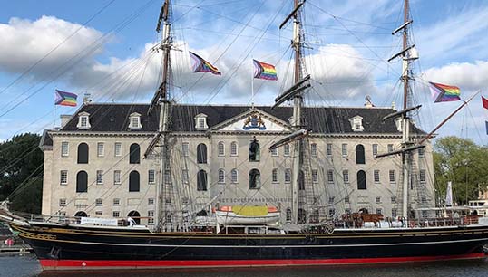 The Netherlands National Maritime Museum with the clipper Stad Amsterdam flying the LGBT+ Pride rainbow flag in August 2021. Image: courtesy of museum Image:The Netherlands National Maritime Museum with the clipper Stad Amsterdam flying the LGBT+ Pride rainbow flag in August 2021. Image: courtesy of museum